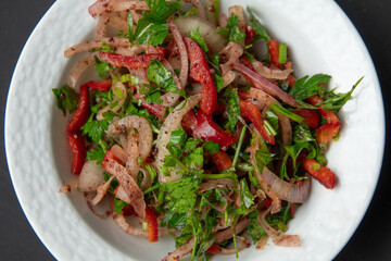 Salad with onion, parsley, red pepper 
sumach and tomatoes in porcelain bowl on dark background. Appetizer for Turkish pizza, pita pizza Lahmacun