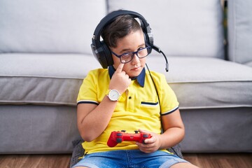 Young hispanic kid playing video game holding controller wearing headphones pointing to the eye...