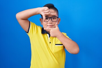 Young hispanic kid standing over blue background smiling making frame with hands and fingers with...