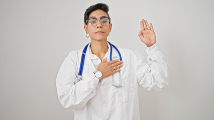 Young beautiful hispanic woman doctor making an oath with hand on chest over isolated white...