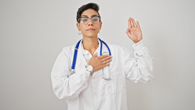 Young beautiful hispanic woman doctor making an oath with hand on chest over isolated white background
