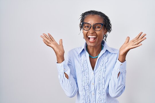 African woman with dreadlocks standing over white background wearing glasses celebrating crazy and amazed for success with arms raised and open eyes screaming excited. winner concept