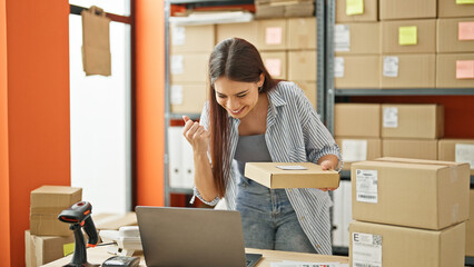 Young beautiful hispanic woman ecommerce business worker using laptop holding package celebrating at office