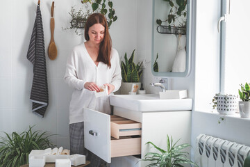 Happy young woman standing near dressing table and taking out a beauty cosmetic from drawer.