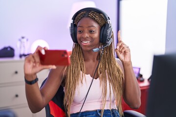 African american woman with braided hair playing video games with smartphone smiling with an idea...