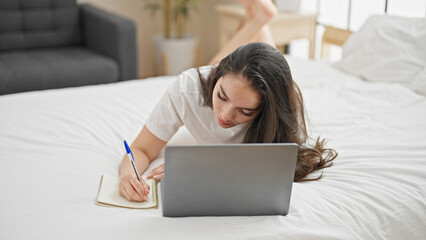 Young beautiful hispanic woman using laptop taking notes at bedroom