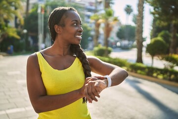 African american woman wearing sportswear looking stopwatch at street