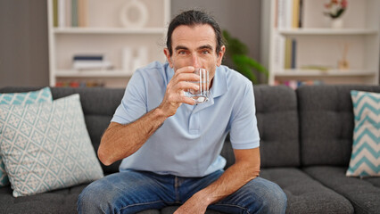 Middle age man drinking glass of water sitting on sofa at home