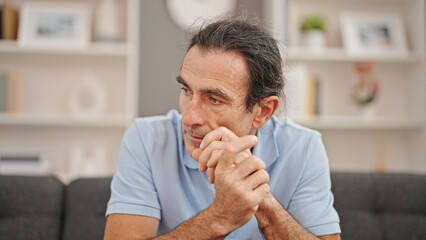 Middle age man sitting on sofa with serious expression at home