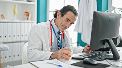 Middle age man doctor holding bottle of pills at the clinic