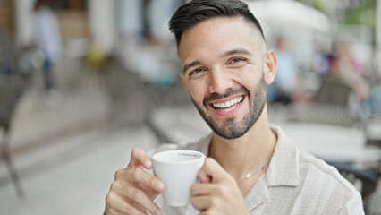 Young hispanic man smiling confident drinking coffee at coffee shop terrace