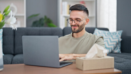 Fototapeta premium Young hispanic man using laptop sitting on floor smiling at home