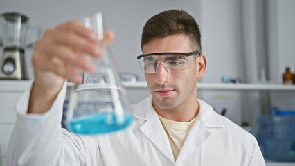 Handsome young hispanic scientist engrossed in medical analysis, looking at test tube while working...