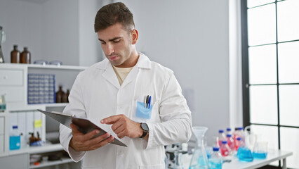 Attractive young hispanic man engrossed in reading a crucial lab report, standing amidst a whirl of science, medicine, and technology in a professional laboratory setting.