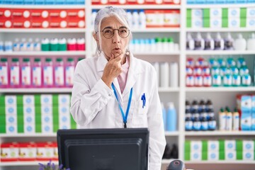 Middle age woman with tattoos working at pharmacy drugstore looking fascinated with disbelief, surprise and amazed expression with hands on chin