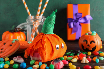 Paper pumpkins for Halloween and tasty candies on wooden table, closeup