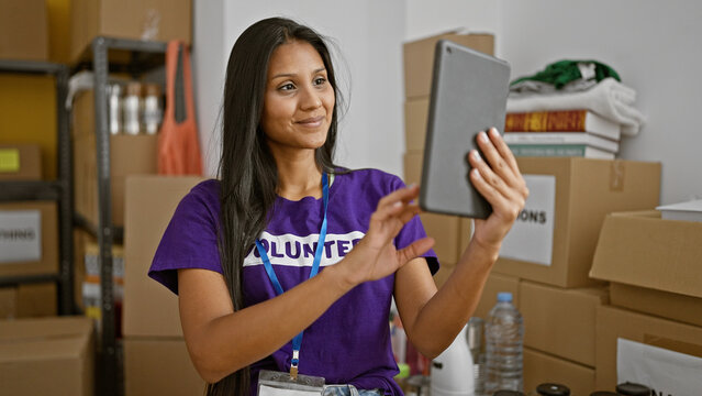 Young latin woman volunteer using touchpad smiling at charity center
