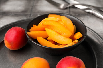 Plate with sweet apricots and bowl of pieces on grey tile background