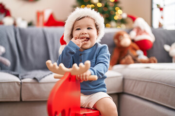Fototapeta na wymiar Adorable caucasian baby playing with reindeer rocking by christmas tree at home