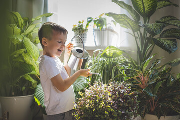 A child in home clothes waters indoor plants from a beautiful stylish metal watering can. 