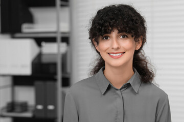 Portrait of confident entrepreneur indoors. Beautiful lady with curly hair smiling and looking into camera. Space for text