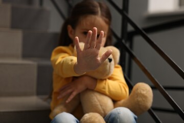 Child abuse. Little girl with teddy bear doing stop gesture indoors, selective focus