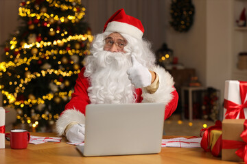 Santa Claus showing thumb up while signing Christmas letters at home