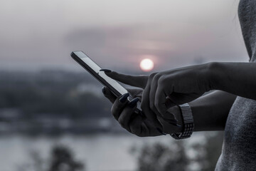 Close up view of woman with long nails using smart phone during sunset near the river. During the...