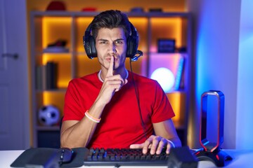 Young hispanic man playing video games asking to be quiet with finger on lips. silence and secret...