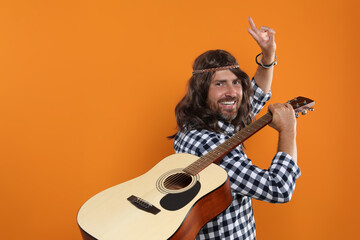 Hippie man with guitar showing V-sign on orange background, space for text