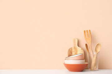 Fototapeta na wymiar Kitchen utensils and bowls on wooden table near beige wall