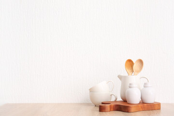 Fototapeta na wymiar Set of crockery and kitchen utensils on wooden table near white wall
