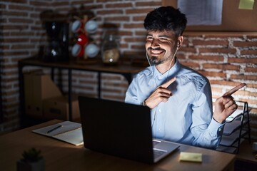 Young hispanic man with beard working at the office at night smiling and looking at the camera...