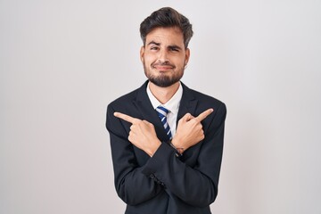 Young hispanic man with tattoos wearing business suit and tie pointing to both sides with fingers, different direction disagree