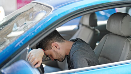 Young hispanic man driving car stressed at street