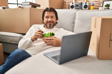 Middle age man using laptop eating salad at new home