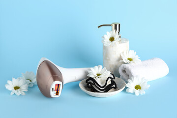 Modern photoepilator with bath supplies and beautiful flowers on blue background