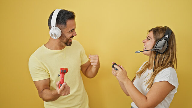 Man and woman couple playing video game celebrating over isolated yellow background