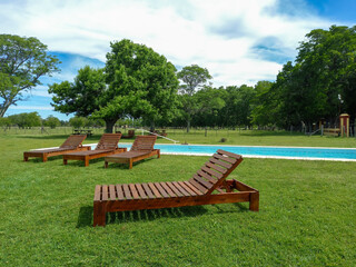 Deckchairs on the lawn beside the swimming pool for relaxation in a tranquil meadow full of trees