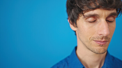 Young hispanic man breathing with closed eyes over isolated blue background