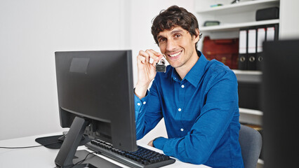 Young hispanic man real state agent using computer holding keys of new home at the office