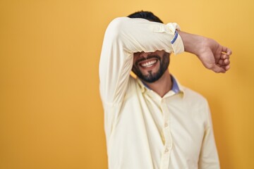Hispanic young man wearing business clothes and glasses covering eyes with arm smiling cheerful and funny. blind concept.