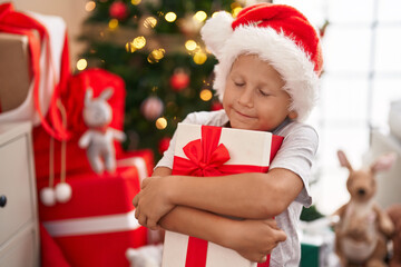 Adorable toddler hugging gift standing by christmas tree at home