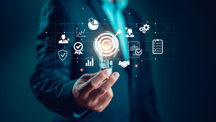 Naklejka premium Businessman holding lightbulb with business goal and target icon, corporate development and global business leadership, success, strategy, prospects, sustainable goals. Ideas in business, inspiration