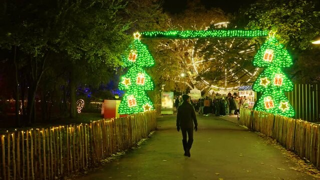 Behind tourist walking into a Christmas Market with Ferris Wheel and winter tree lights illuminated in  Vienna, Austria
