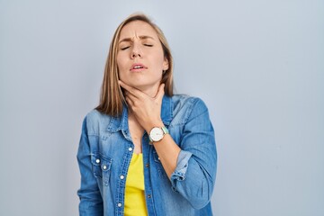 Young blonde woman standing over blue background touching painful neck, sore throat for flu, clod...