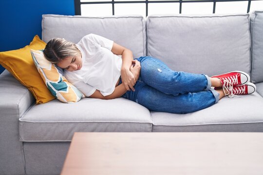 Young blonde woman suffering for menstrual pain lying on sofa at home