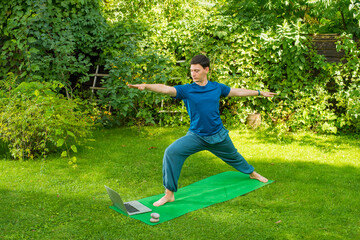 yoga man on a natural green background performs exercises using a laptop