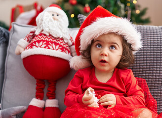 Adorable hispanic girl sitting on sofa by christmas tree at home