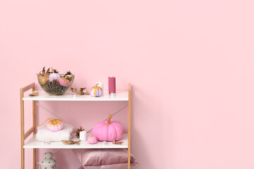 Painted pumpkins with beautiful decorations and burning candles on shelving unit in room